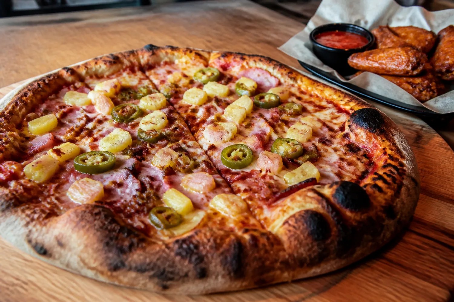 Hot Hawaiian wood-fired pizza with wings on a wood table